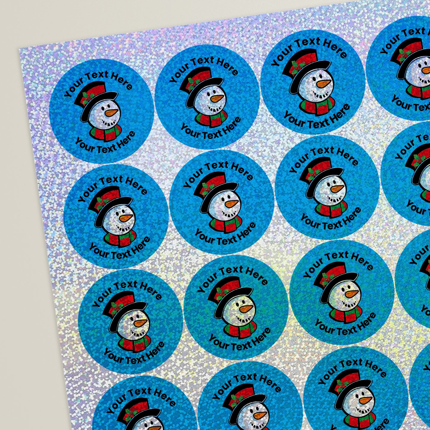 Sheet of round, holographic cyan stickers, each featuring a smiling snowman head with hop hat at the centre. Surrounding is placeholder text reading 'Your text here' above and below, indicating customisable areas for personalised messages