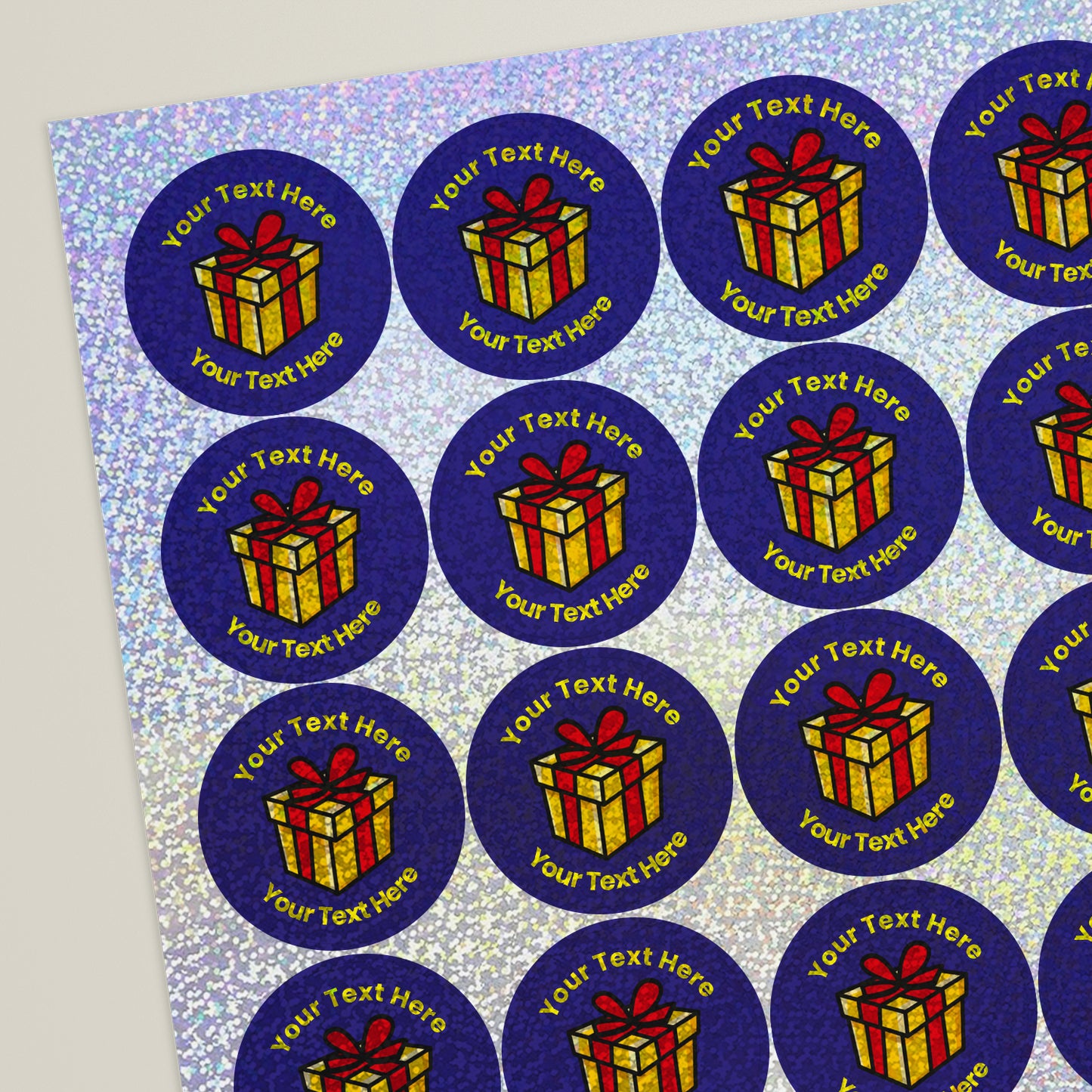 Sheet of round purple holographic stickers featuring a shining gold present with red ribbon in the centre. Each sticker has placeholder text reading 'Your text here' curved above and below the illustration.