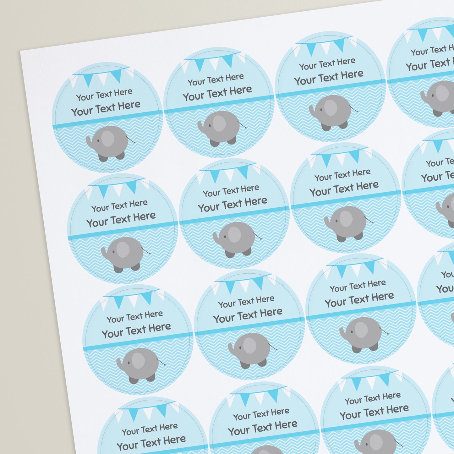 Sheet of round pale blue stickers with a line halfway down the sticker. The bottom half shows a grey elephant against a wavy background. Above the line placeholder text reading 'Your text Here' with two tone bunting at the top of the sticker. Ideal for customisation for baby showers.