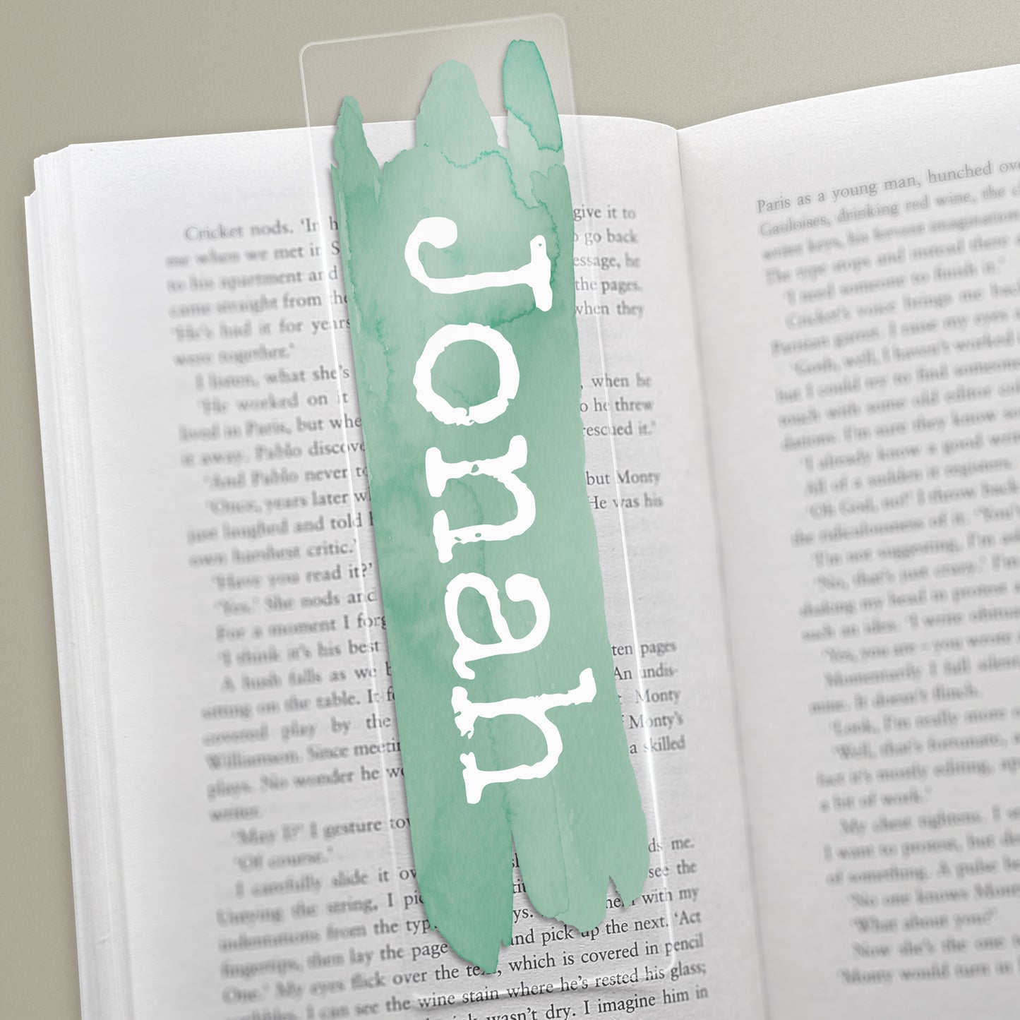 A clear acrylic bookmark with the name 'Jonathan' printed in green brushstroke text on a book page.