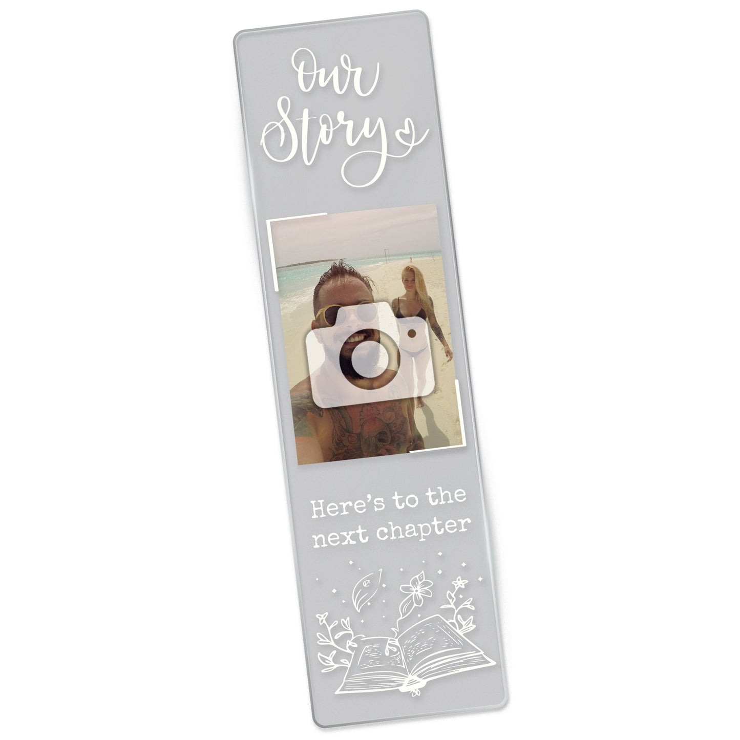 Clear acrylic holiday themed bookmark featuring the phrase 'Our Story' at the top, a photo of a couple on a beach, and the words 'Here’s to the next chapter' in black font above an illustrated open book with magical elements.