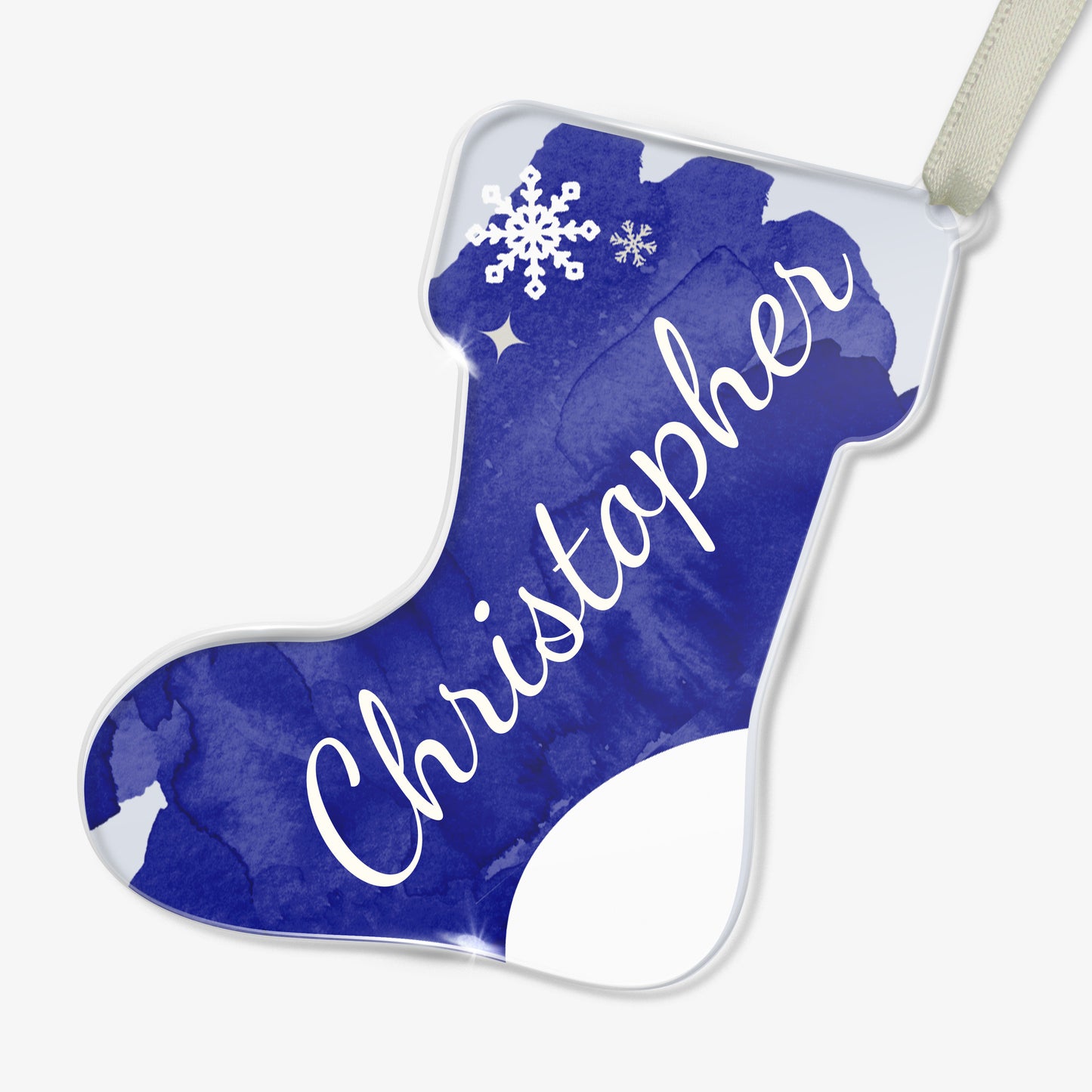 Personalised Christmas stocking-shaped acrylic decoration with the name 'Christopher' written in white script on a dark blue watercolour background, featuring a snowflake design, placed on a white surface beside twine and scissors