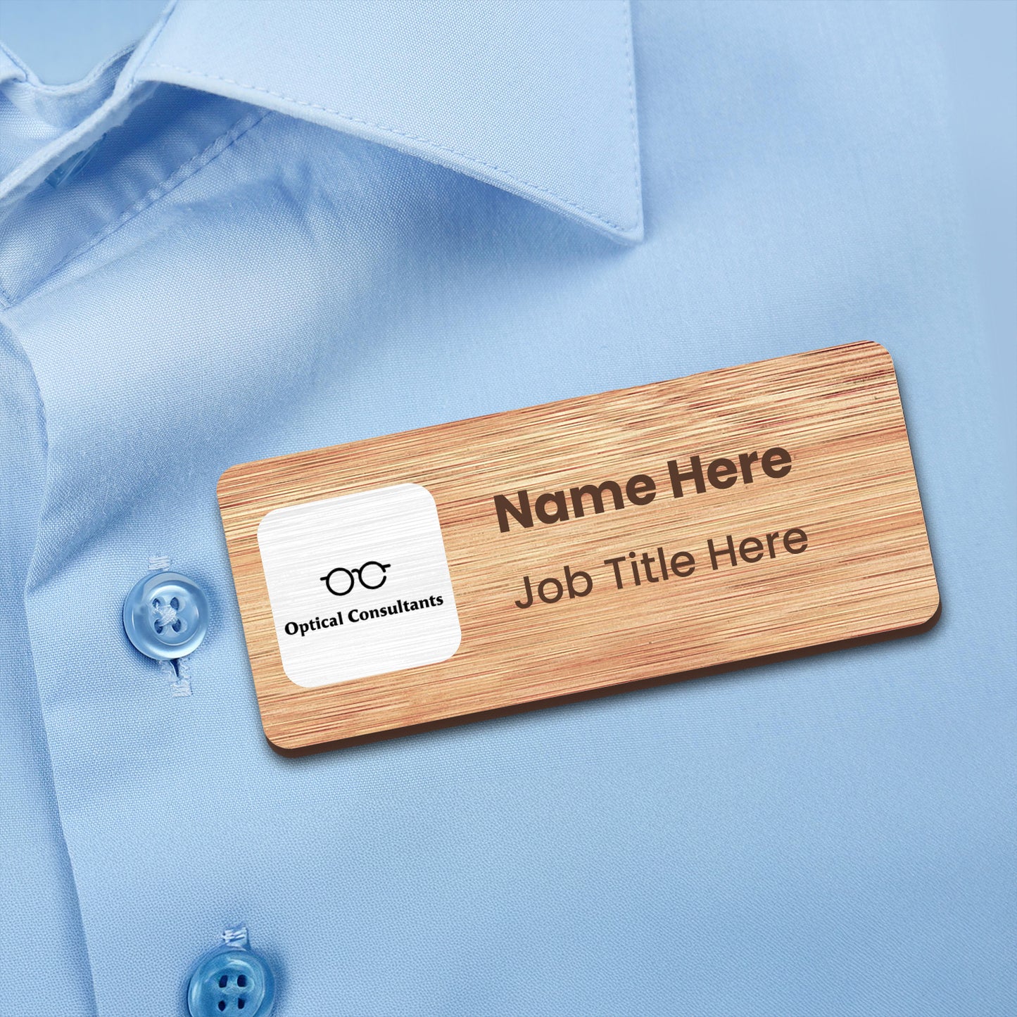 A rectangular bamboo name badge. The front displays the Optical Consultants logo on a white panel, with placeholder text for 'Name Here' and 'Job Title Here'.