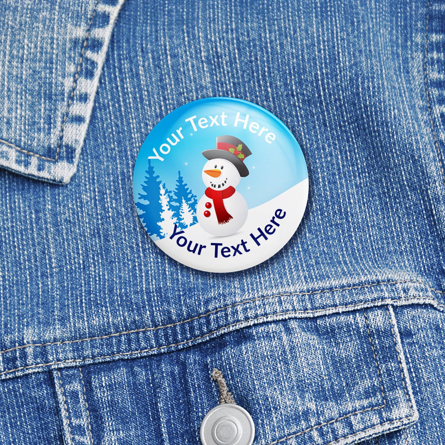 38mm round personalised badges featuring a cheerful snowman wearing a top hat and red scarf, set against a snowy blue background with pine trees; includes customisable text above and below the snowman, equipped with safety pin fastenings—ideal for festive rewards. Placed on a denim jacket.