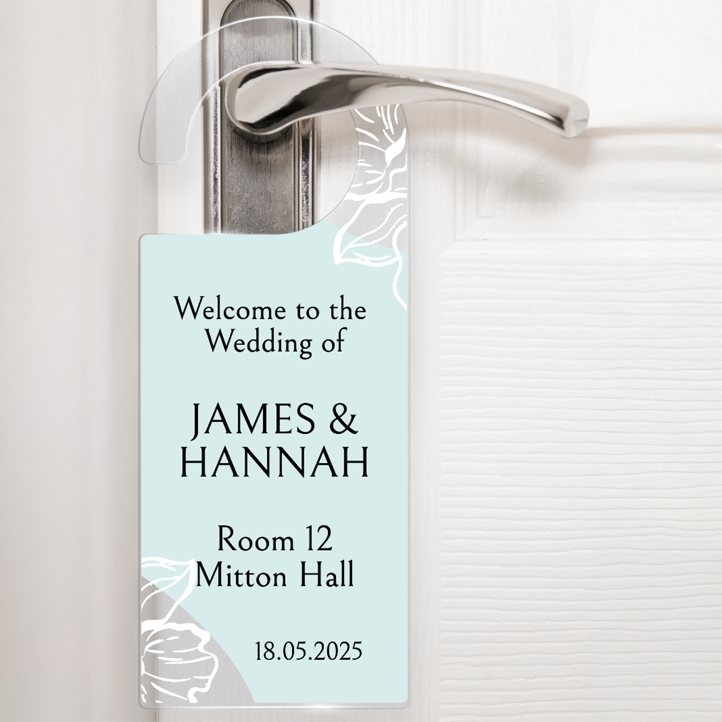 Acrylic door hanger suspended from a silver door handle against a white door. The top wording says 'Welcome to the Wedding of' middle wording 'James & Hannah' Lower wording 'Room 12 Mitton hall' and then bottom right '18.05.2025'. The door hanger has a pale green background with delicate flowers at the handle and the bottom left corner.