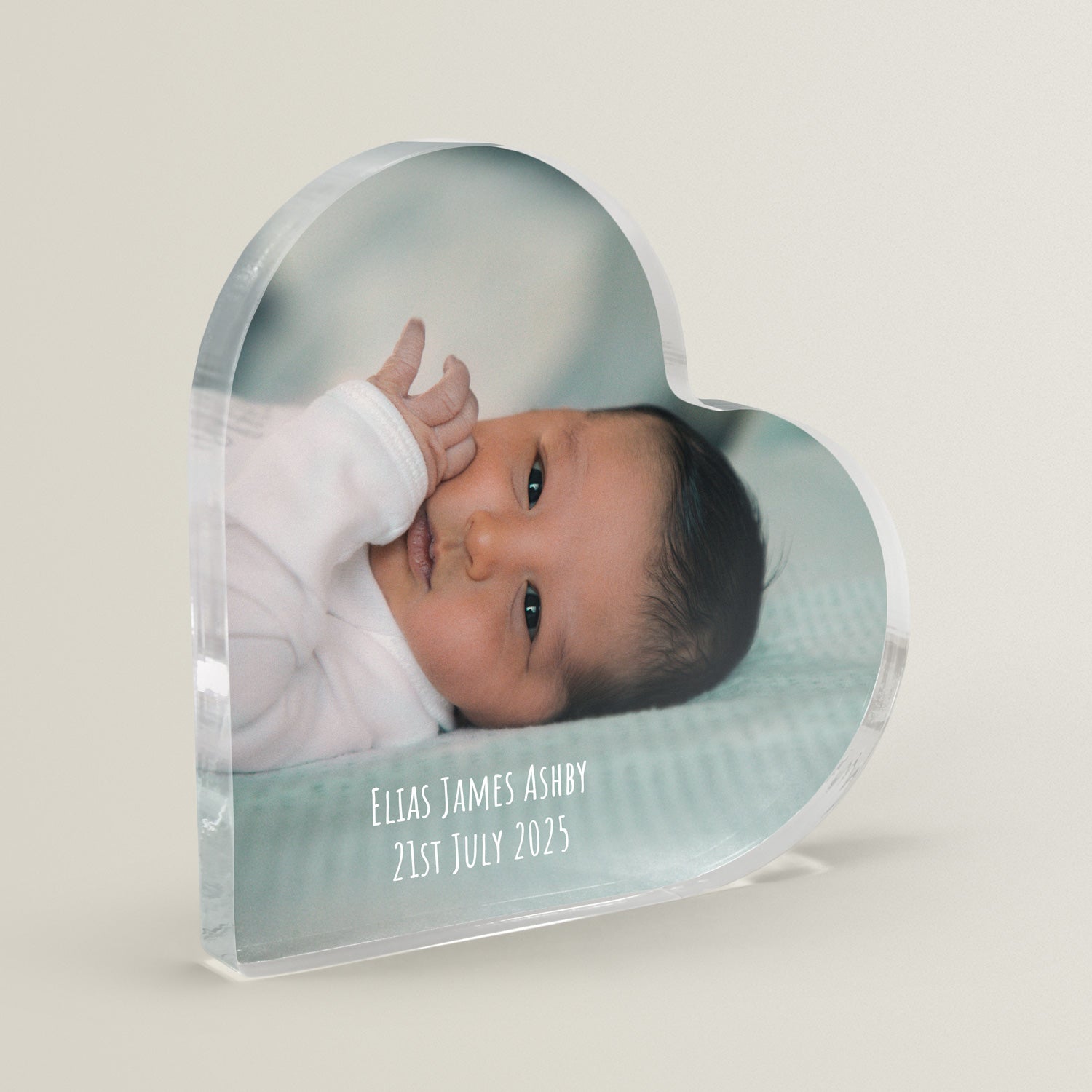 Heart-shaped photo plaque with a baby's face and personalised text on a light cream/grey background.