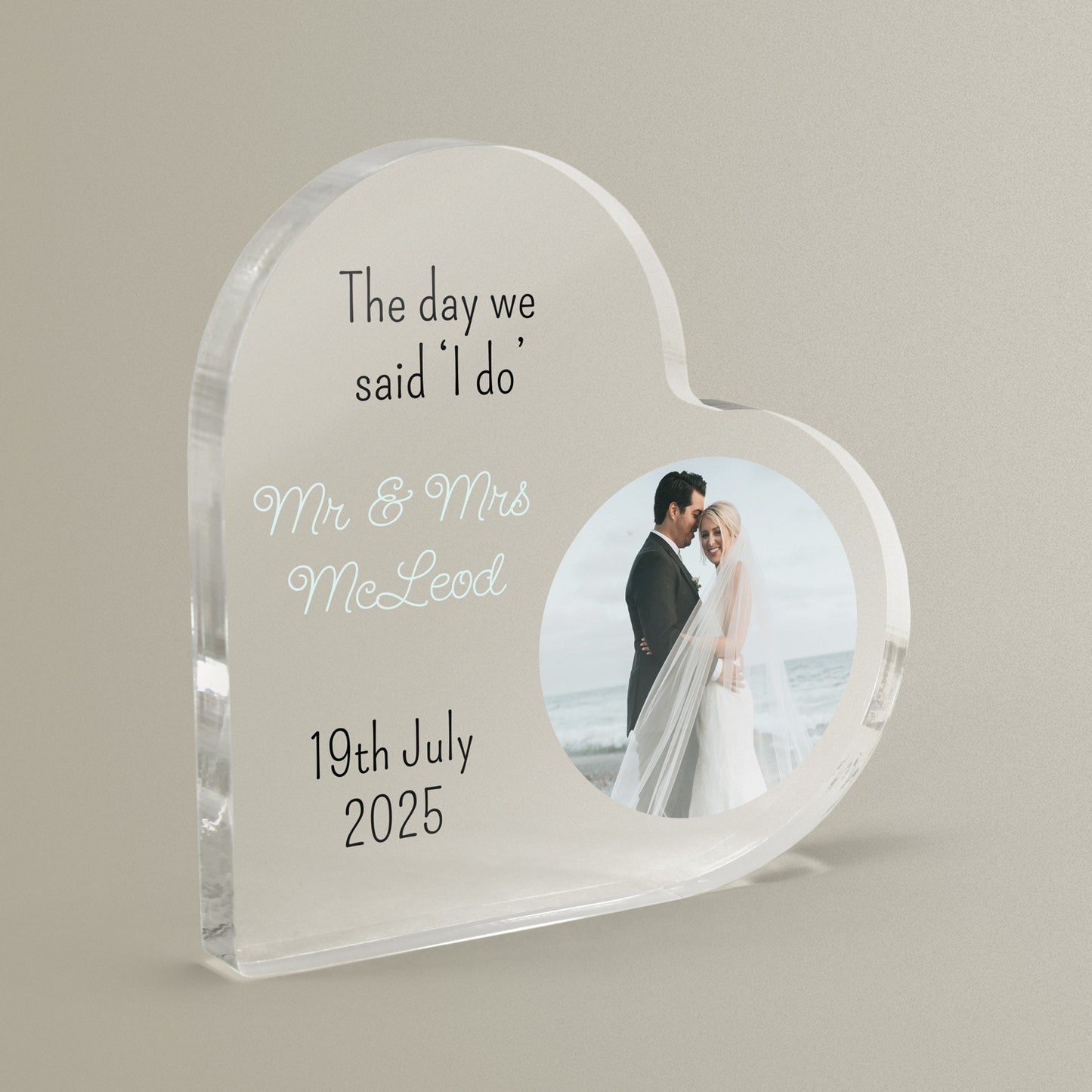 Heart-shaped acrylic block with personalized text and a photo of a couple on their wedding day on a beige background.