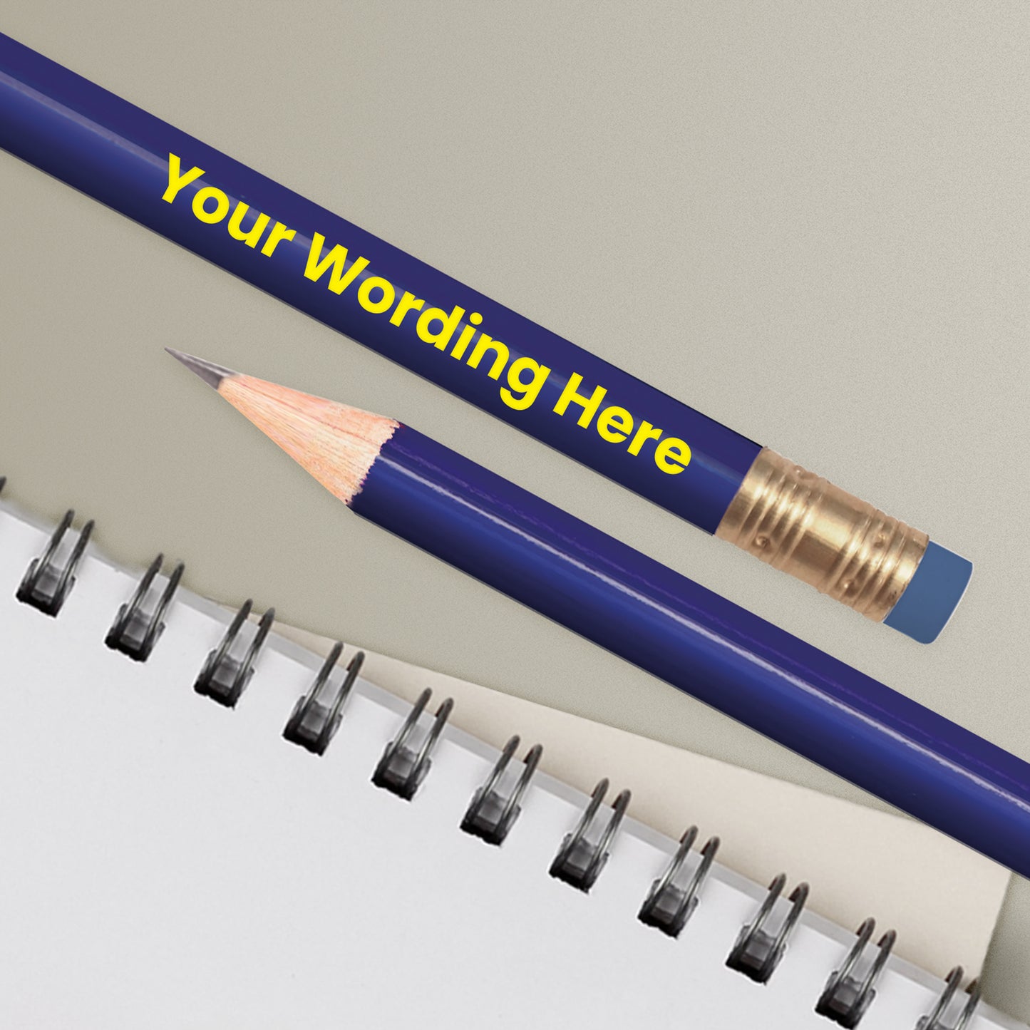 A royal blue HB pencil with customised text 'Your Wording Here' printed on it, positioned next to a notepad with dotted lines.