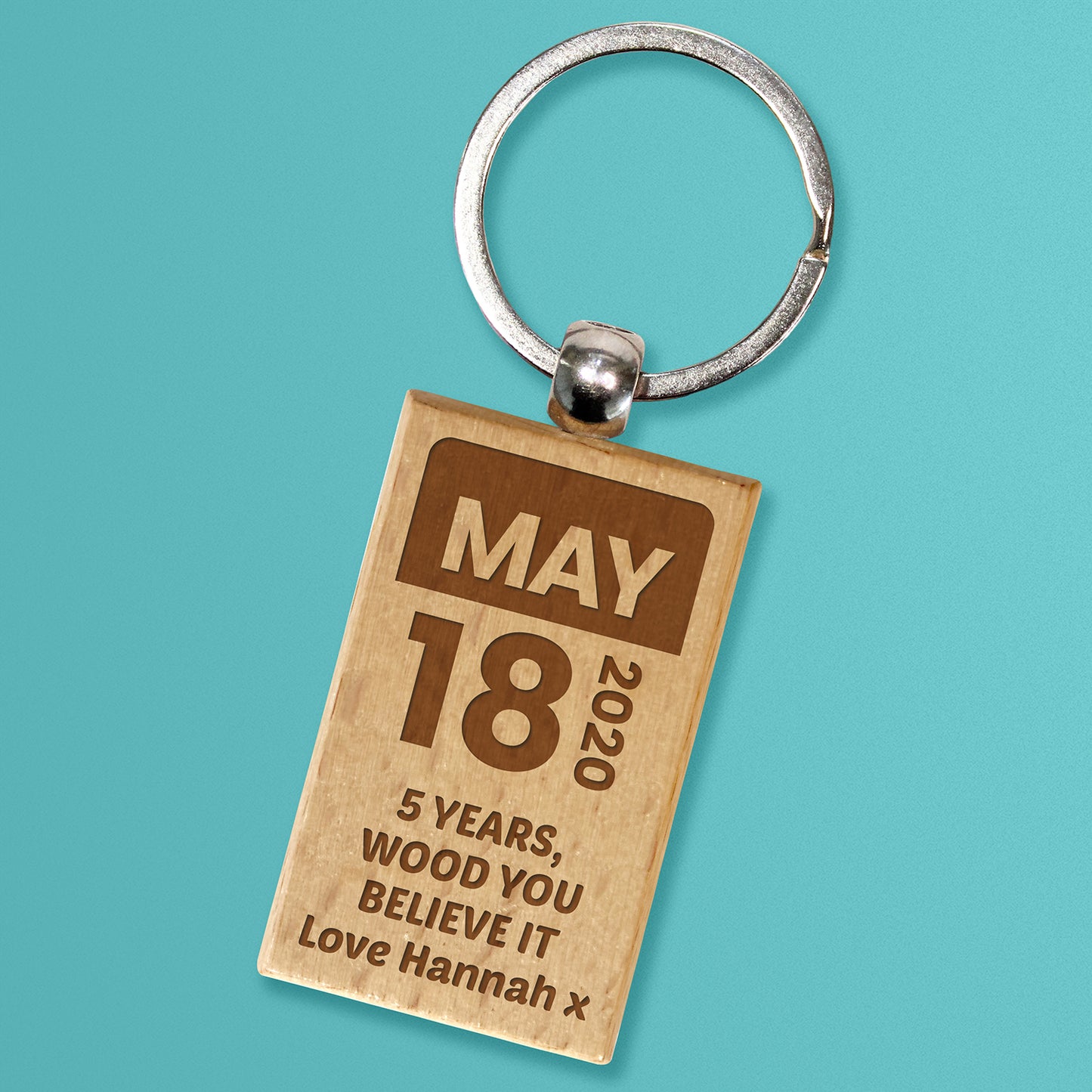 A wooden keyring with a special date 'May 18' and personalized message '5 years, wood you believe it Love Hannah' etched on it, attached to a stainless steel keyring.