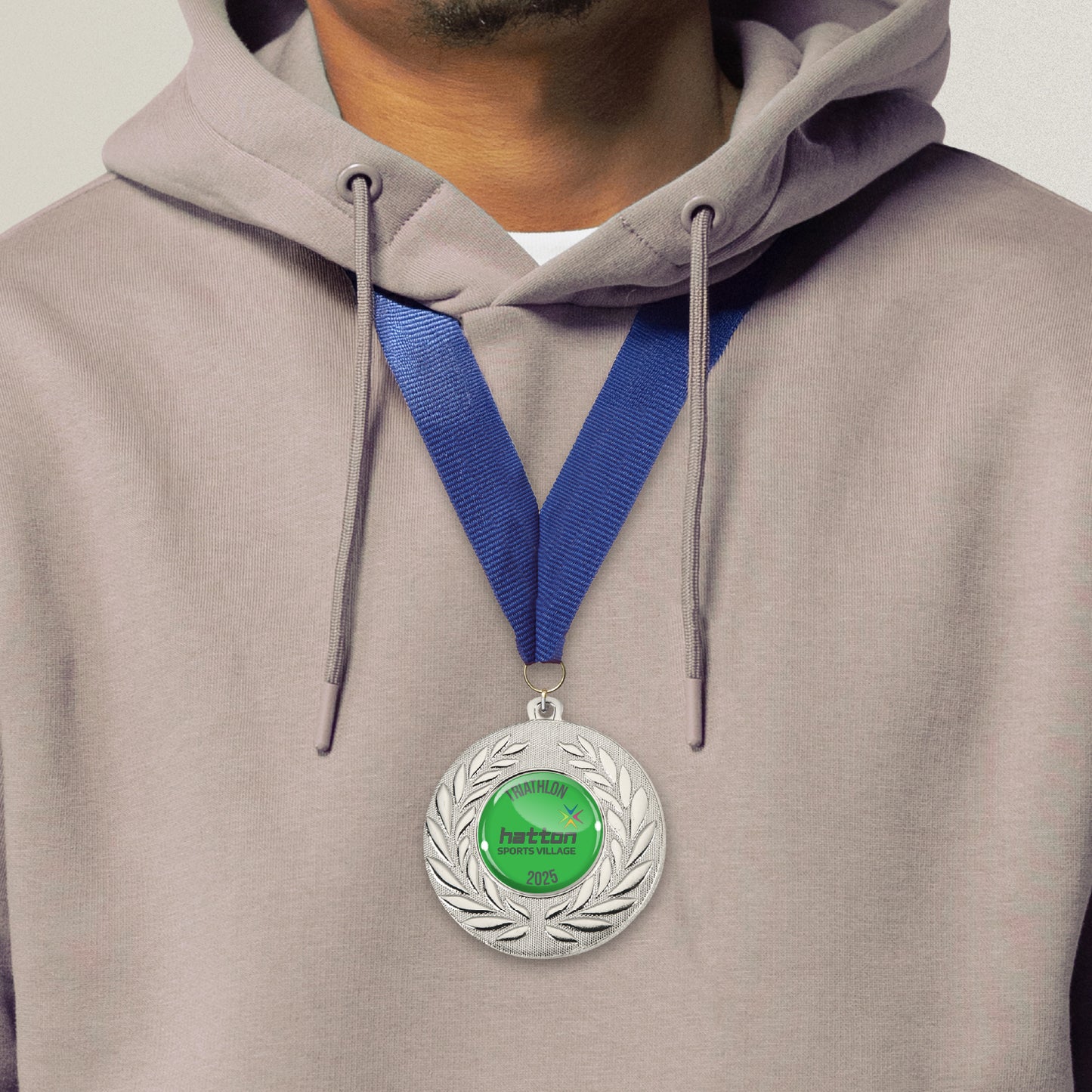 silver-coloured metal medals, each featuring a central 25mm circular area for custom designs, encased in a clear, glossy dome; surrounded by a laurel wreath pattern and attached to a blue ribbon; designed for personalisation with text and images, ideal for sporting events and achievements. Worn by a man after partaking in a triathlon.
