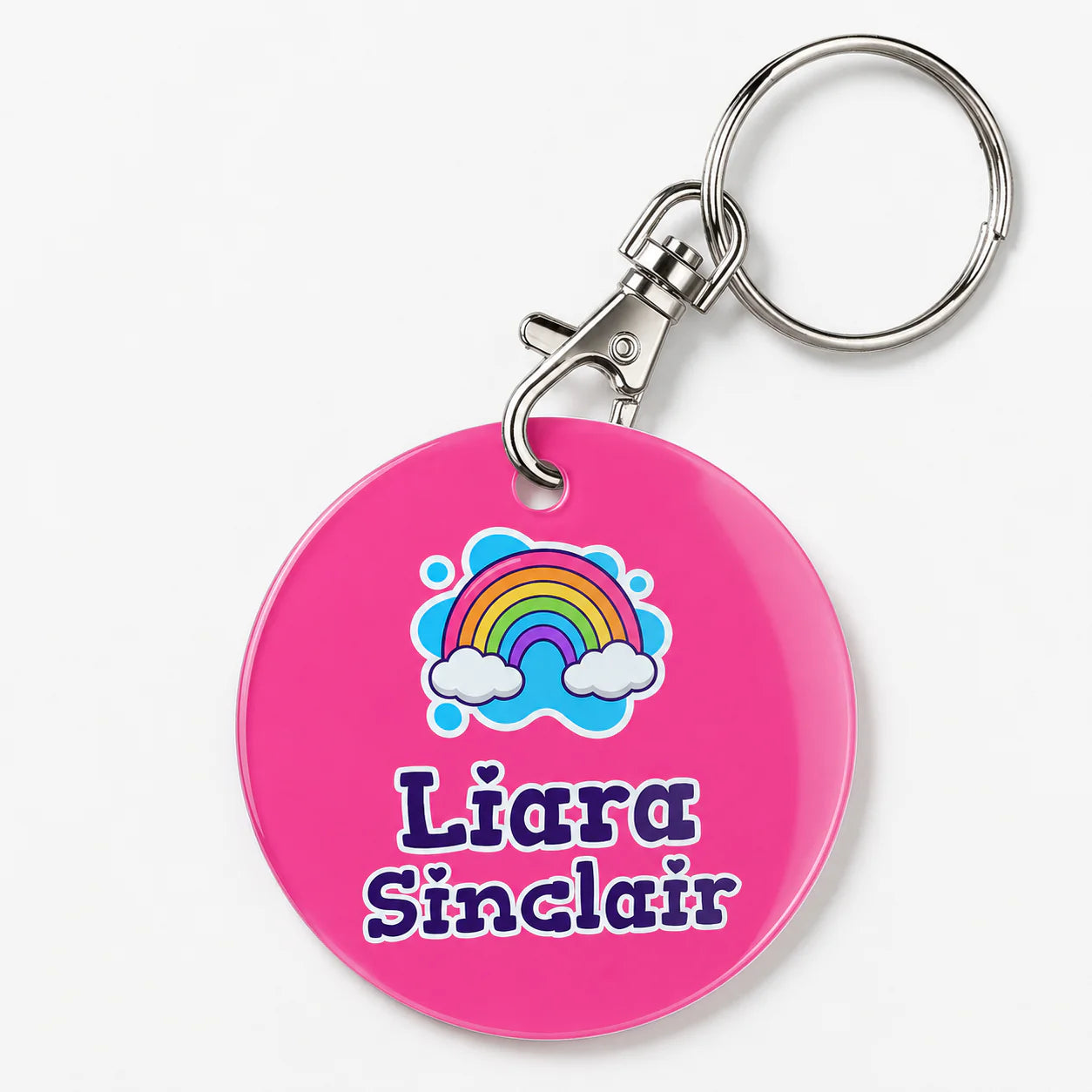 A pink keychain featuring a colorful rainbow and cloud graphic above the personalized name 'Liara Sinclair' in purple.