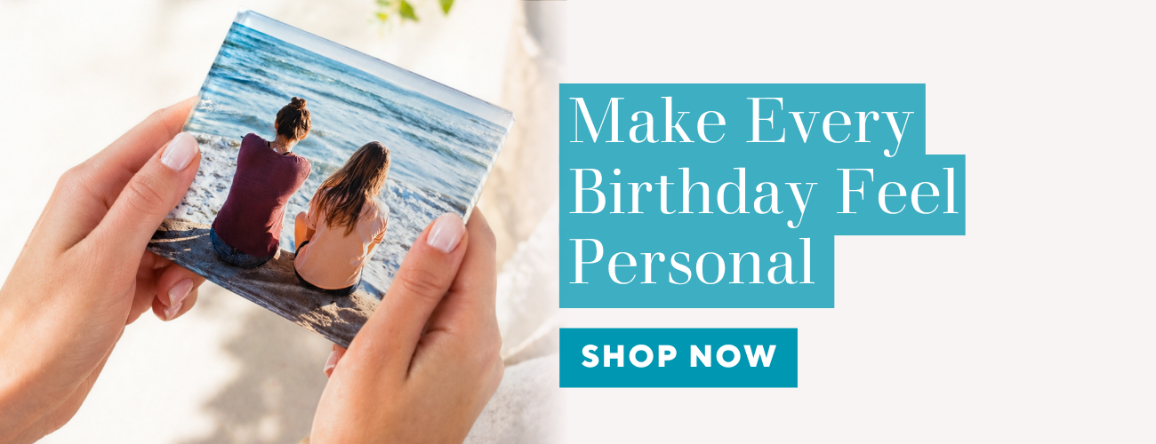 Person holding a photo of two people on a beach with promotional text 'Make Every Birthday Feel Personal' and 'Shop Now' button.