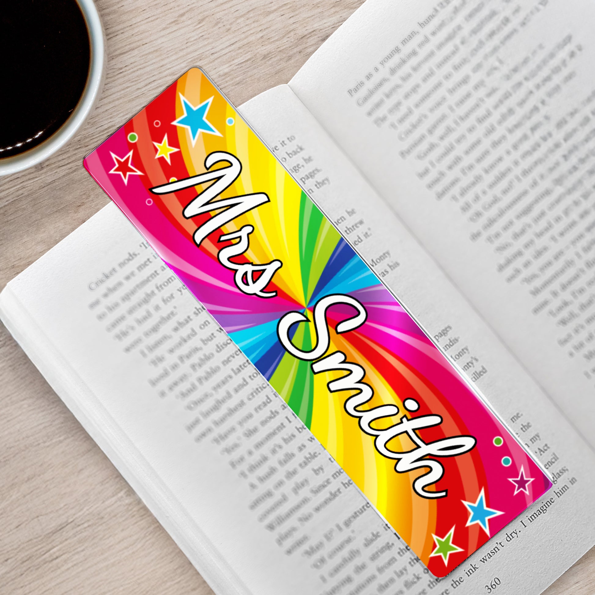 Personalised “Mrs Smith” acrylic bookmark with bright rainbow star design, shown resting across the pages of an open book.