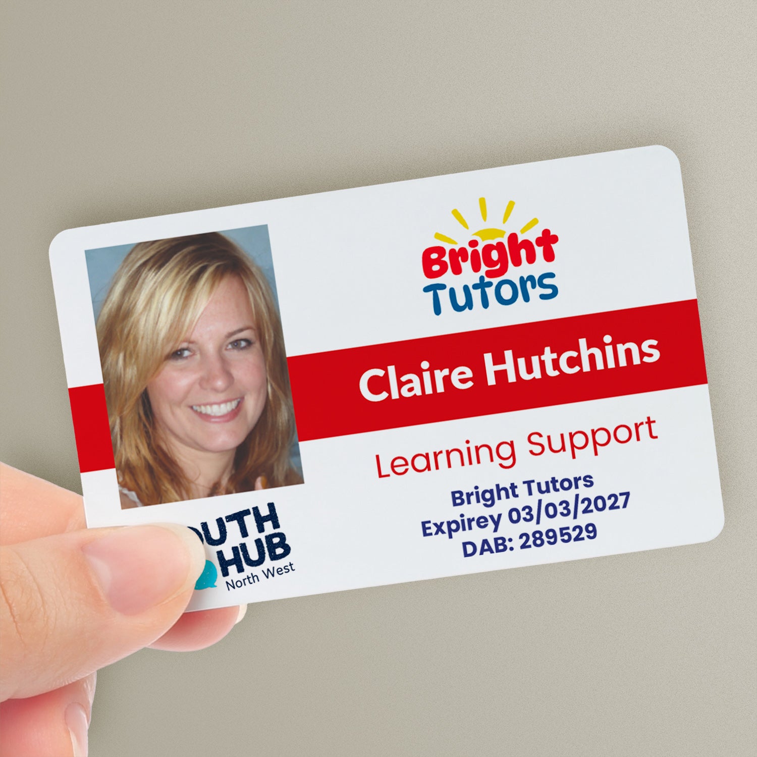 A personalised tutor ID card with a photo, company logo, trust logo, and custom text. The ID card is held in a hand and has a red colour strip - with the name 'Claire Hutchins' and the title 'Learning Support'.