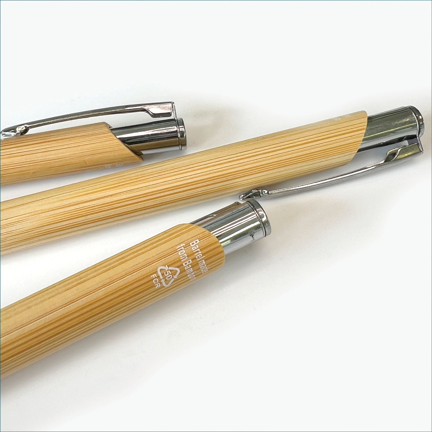 Close-up of several bamboo ballpoint pens, highlighting the natural wood-grain finish, metal clips and recycled material marking.