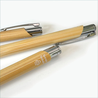 Close-up of several bamboo ballpoint pens, highlighting the natural wood-grain finish, metal clips and recycled material marking.