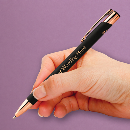Black personalised pen with rose gold detailing and engraved wording, shown being held in the hand.