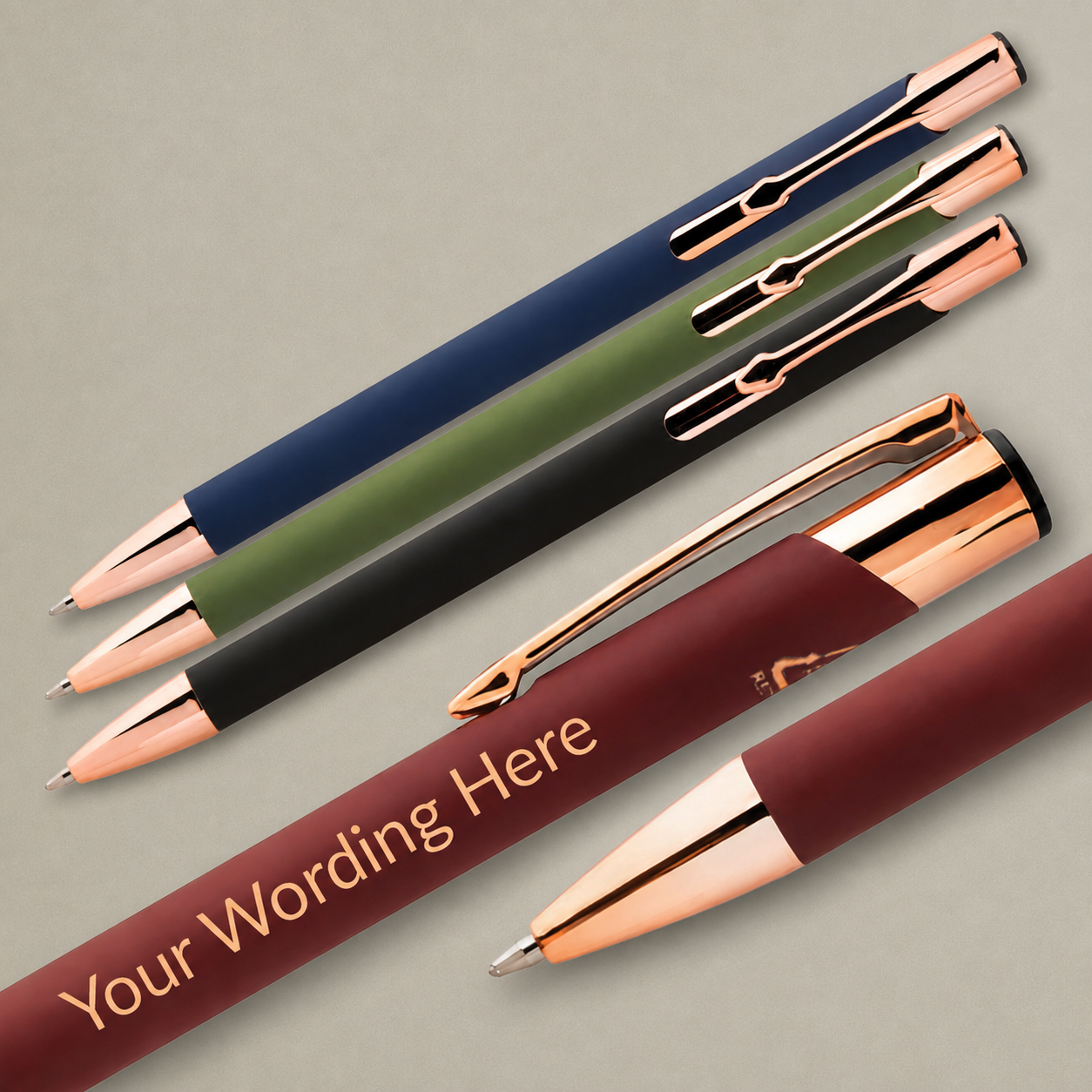 Black, green, navy and burgundy personalised pens with rose gold detailing arranged diagonally on a beige background.
