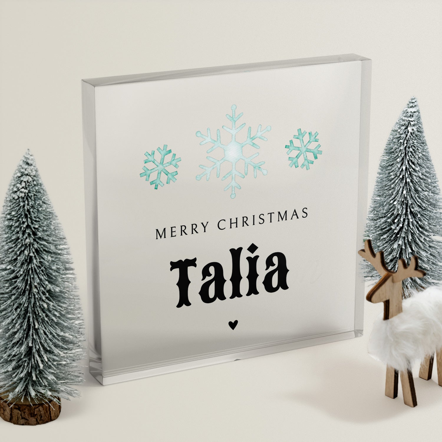 Clear acrylic block with teal snowflakes and 'Merry Christmas Talia' text, surrounded by decorative trees and a deer.