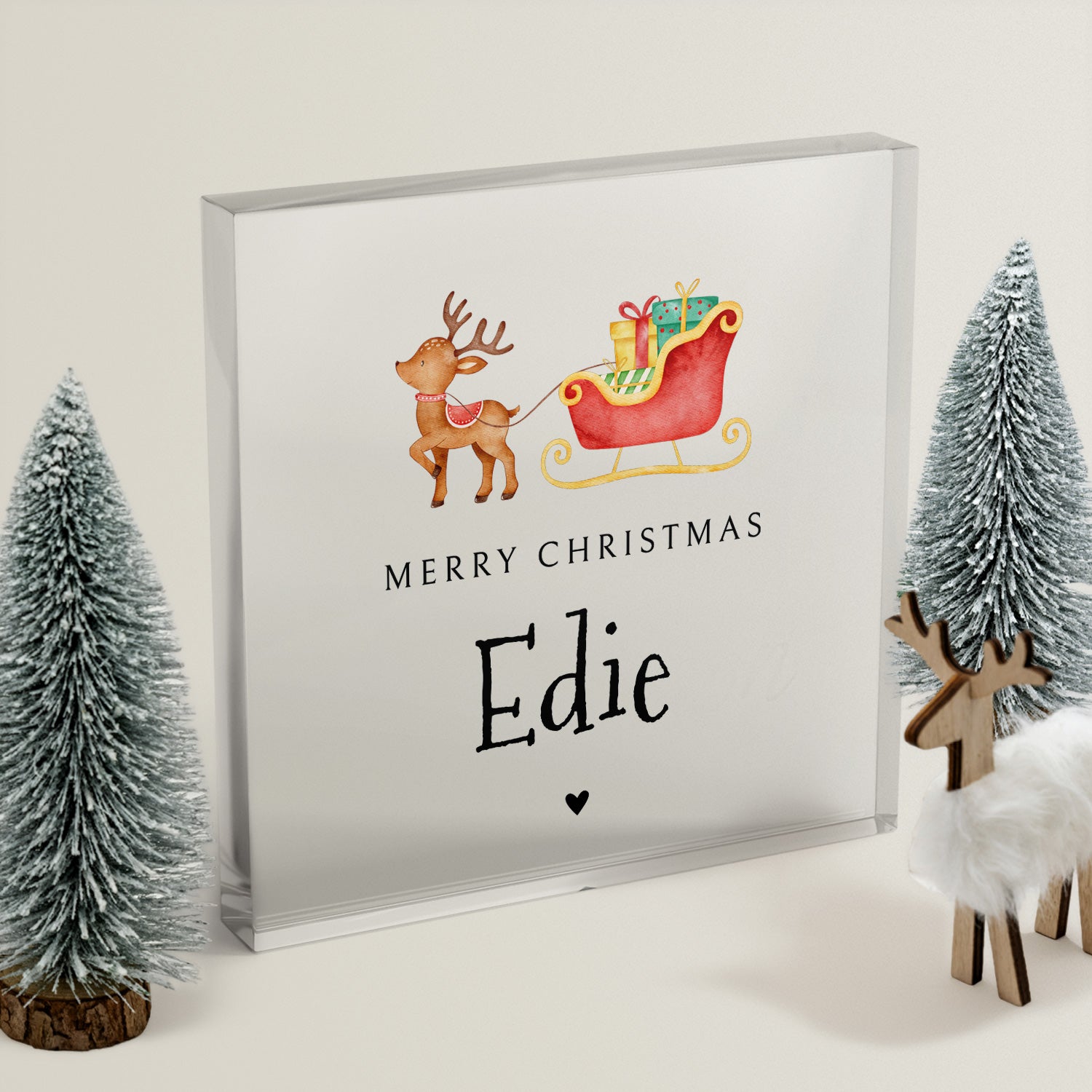 Framed Christmas-themed acrylic block with reindeer and sleigh, surrounded by decorative trees and deer figurines.