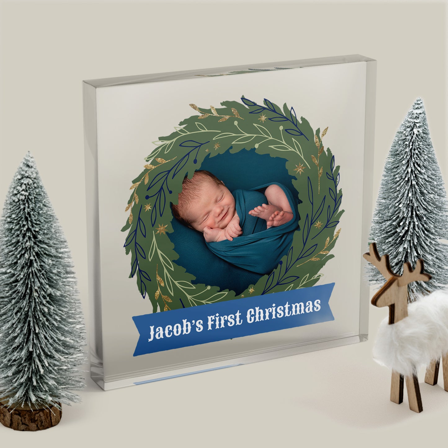 Decorative photo album with a baby in a wreath design, titled 'Jacob's First Christmas', surrounded by festive decorations.