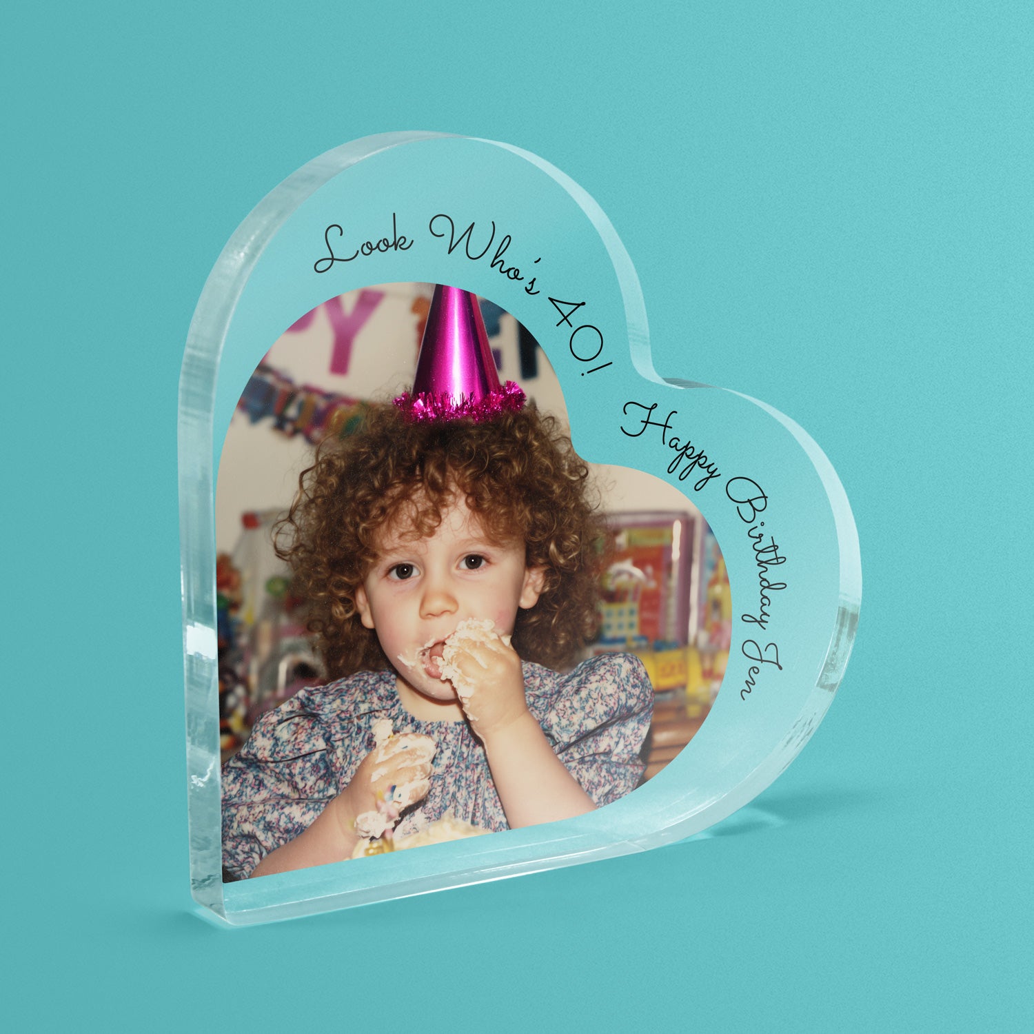Heart-shaped photo block with a child wearing a party hat and personalised text on a teal background.