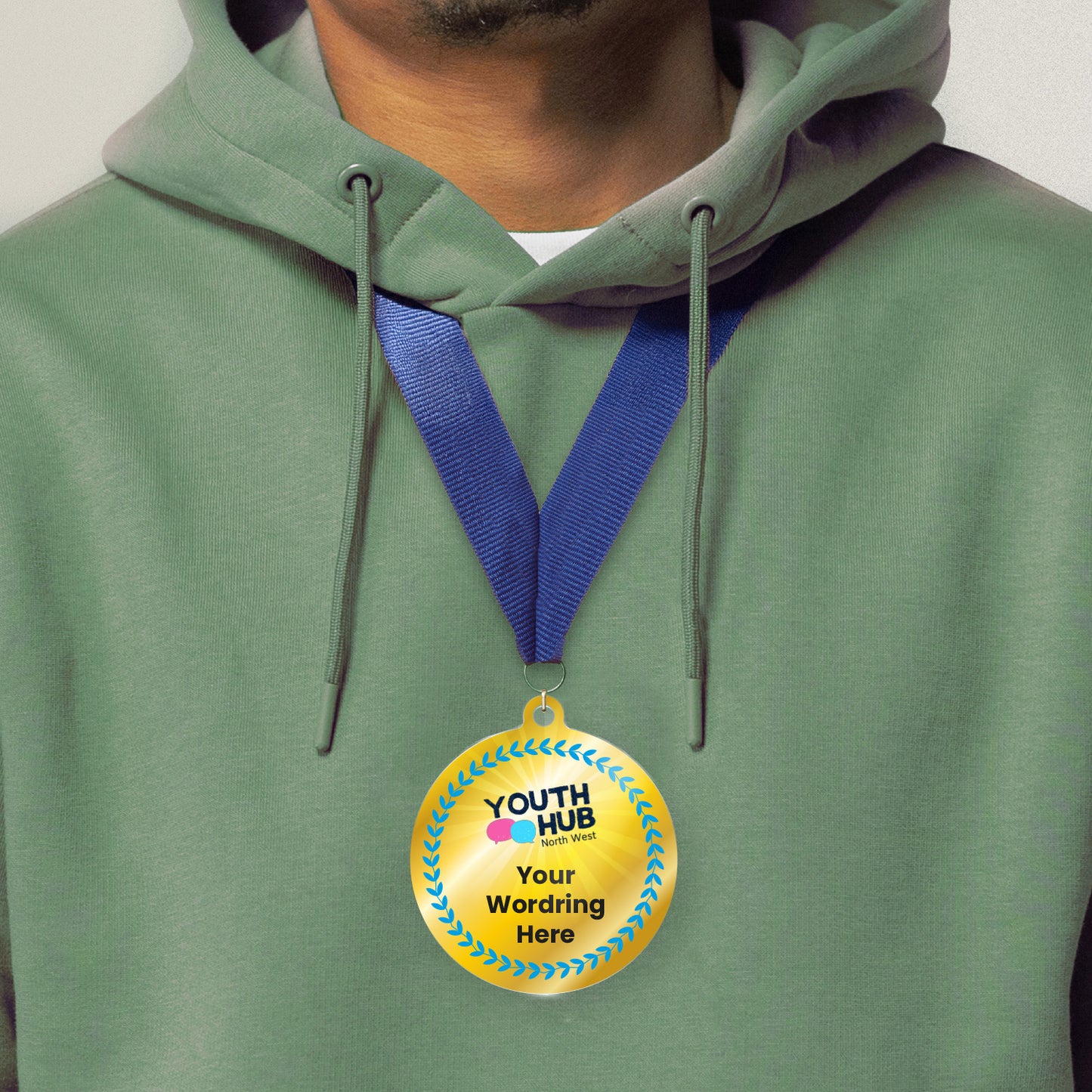 Acrylic personalised medal with blue ribbon showing blue design with blue wreath, Youth Hub logo and personalised wording. Worn around a persons neck wearing a green hoodie.
