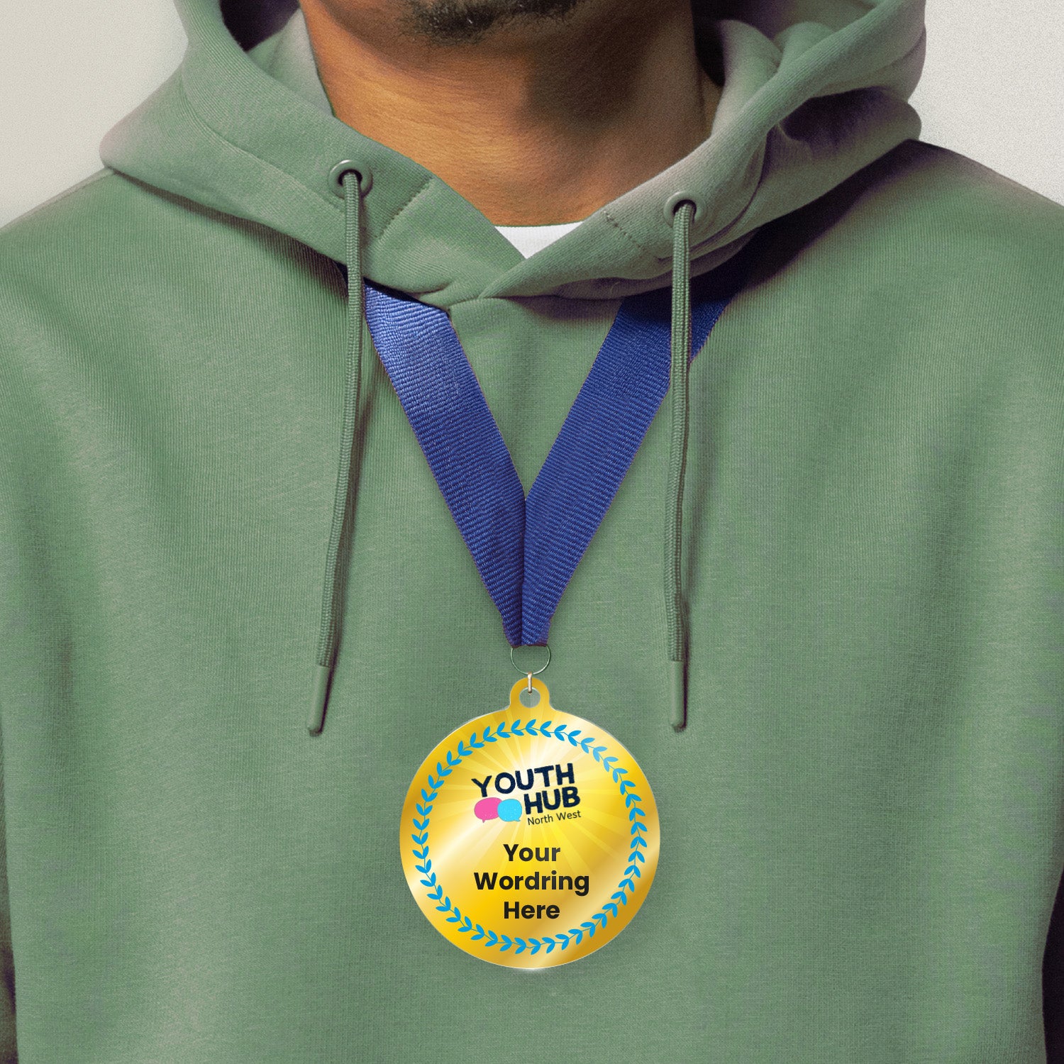 Acrylic personalised medal with blue ribbon showing blue design with blue wreath, Youth Hub logo and personalised wording. Worn around a persons neck wearing a green hoodie.