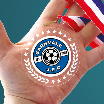 Acrylic personalised medal with stripy ribbon showing clear background with wreath design and 'Garnvale JFC' logo. held in a hand.
