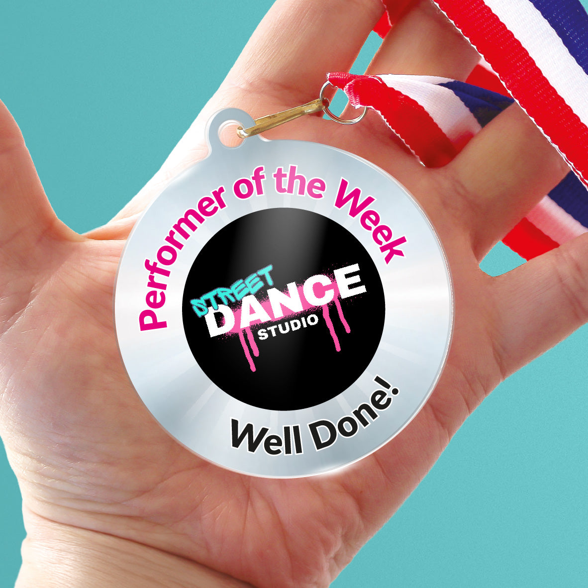 Acrylic personalised medal with stripy ribbon showing silver design with 'Street Dance Studio image' and 'Performer of the Week', 'Well done!' wording. Held in a hand.