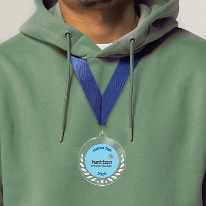 Acrylic personalised medal with blue ribbon showing wreath design with 'Hatton 10K 2026 wording', worn on a person in a green hoodie.