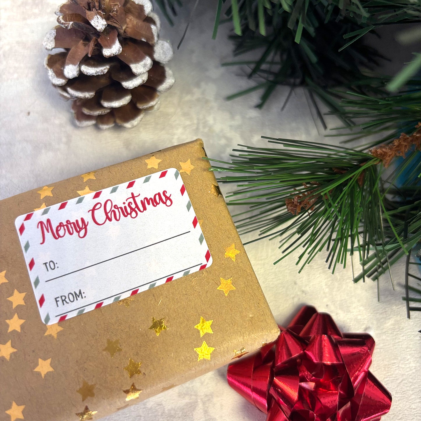 Gift box with 'Merry Christmas' tag, pine cone, and red bow on a snowy background