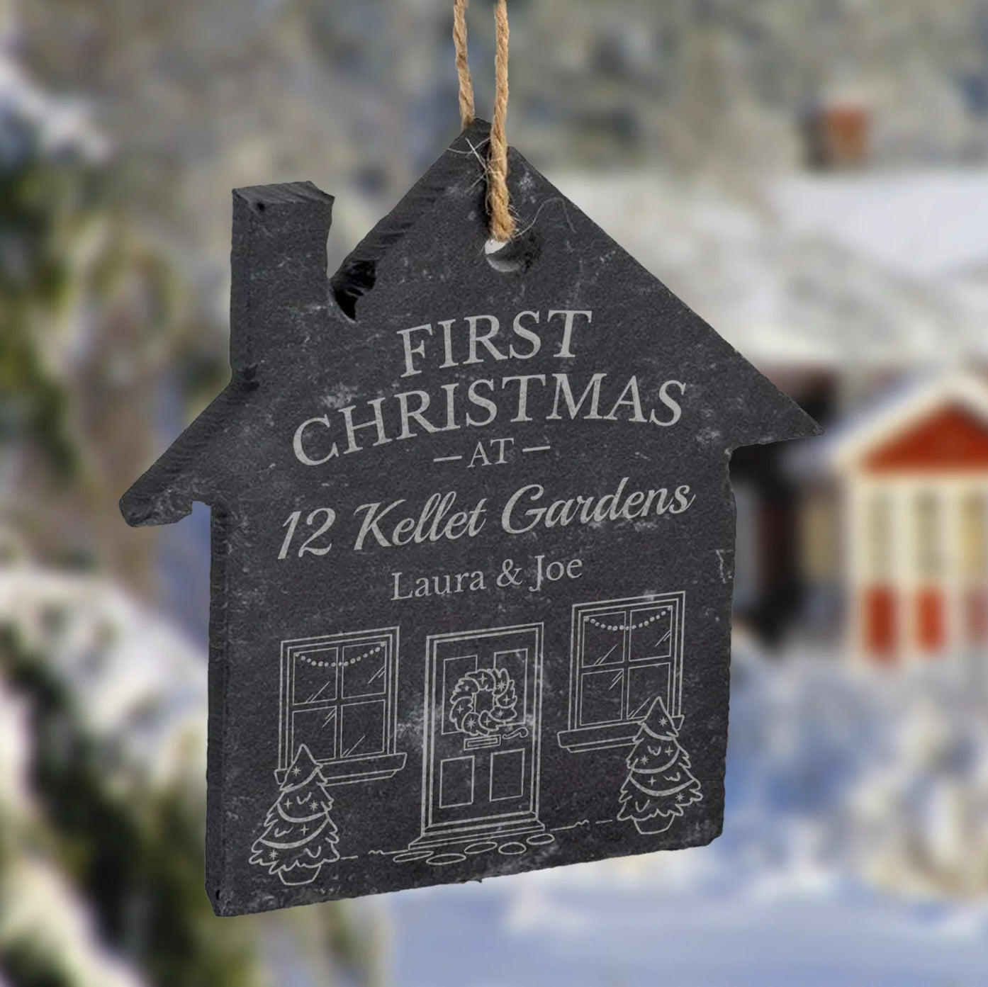 Decorative house-shaped slate ornament etched with 'First Christmas at 12 Kellet Gardens' text, against a snowy background.