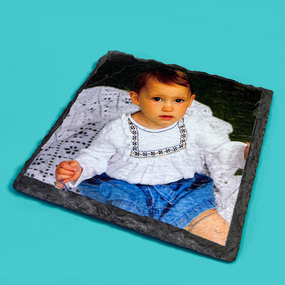 Child in a white blouse and blue pants on a slate coaster with a teal background