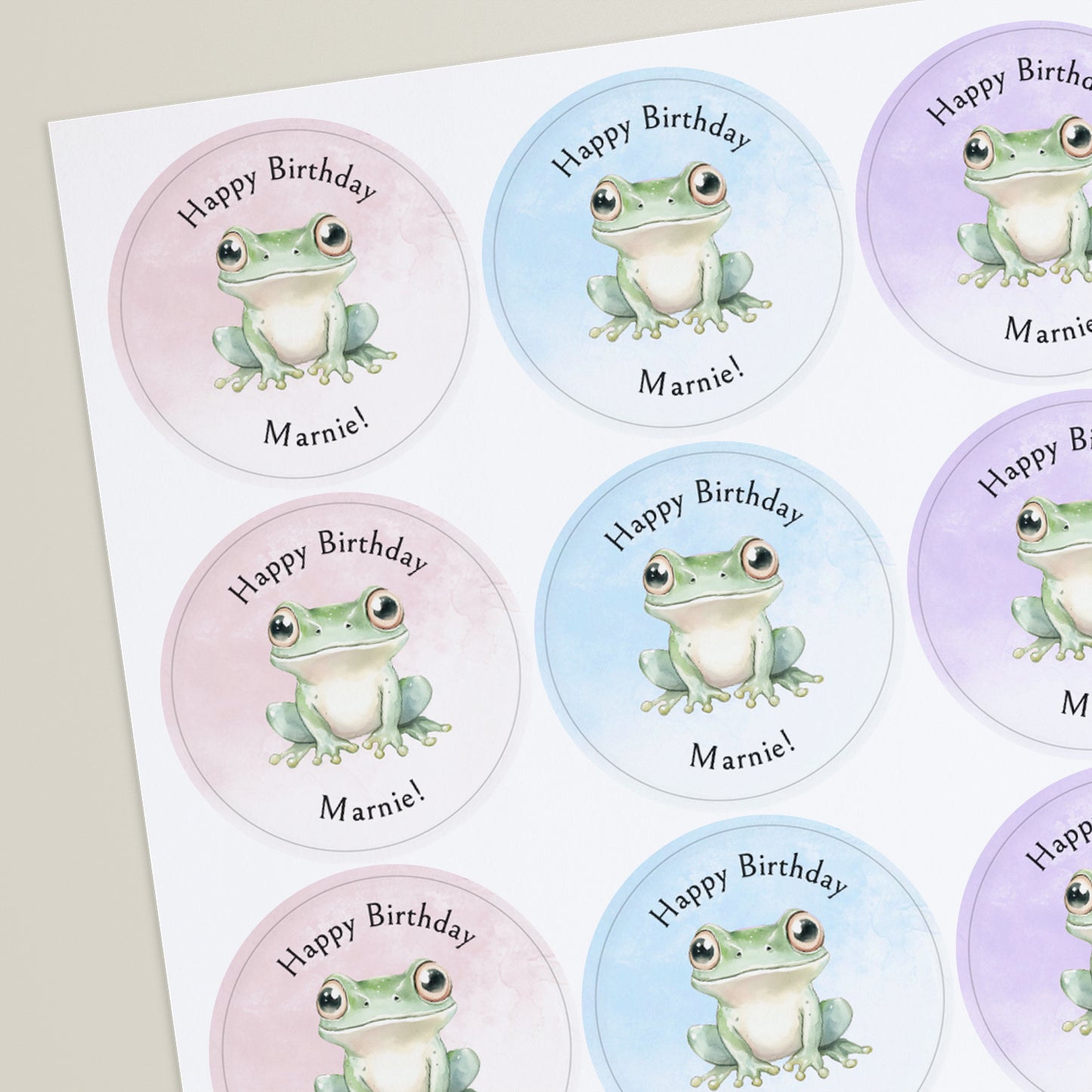 Sheet of round personalised birthday stickers featuring a cute illustrated green frog on pastel backgrounds, with the text “Happy Birthday Marnie!” around each design.