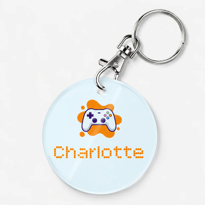 Round keychain with a gaming controller design and the name 'Charlotte' on a light blue background
